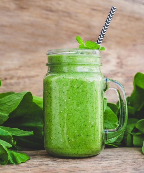 Mason jar mugs filled with green spinach, banana and coconut milk health smoothie with with a spoon of oatmeal on wooden rustic table. Green healthy food concept